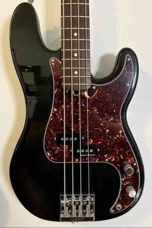 An electric bass hanging on the wall, it's black with a brown tortoise shell pickguard