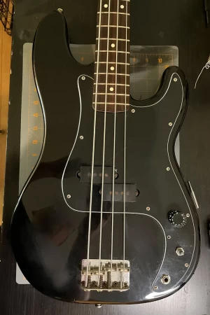 An electric bass hanging on the wall, it's all rusty and scuffed, it's black with a black pickguard